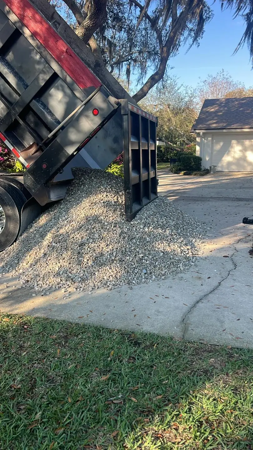 Dump truck unloading a load of gray #57 crushed stone onto a residential driveway in Orlando, Florida