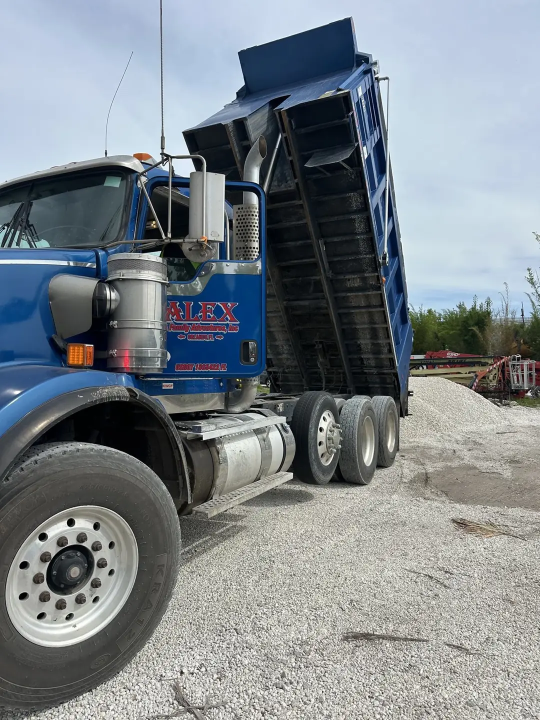 Blue Alex and Family Trucking dump truck with its bed raised on the crushed stone yard in Orlando, Florida