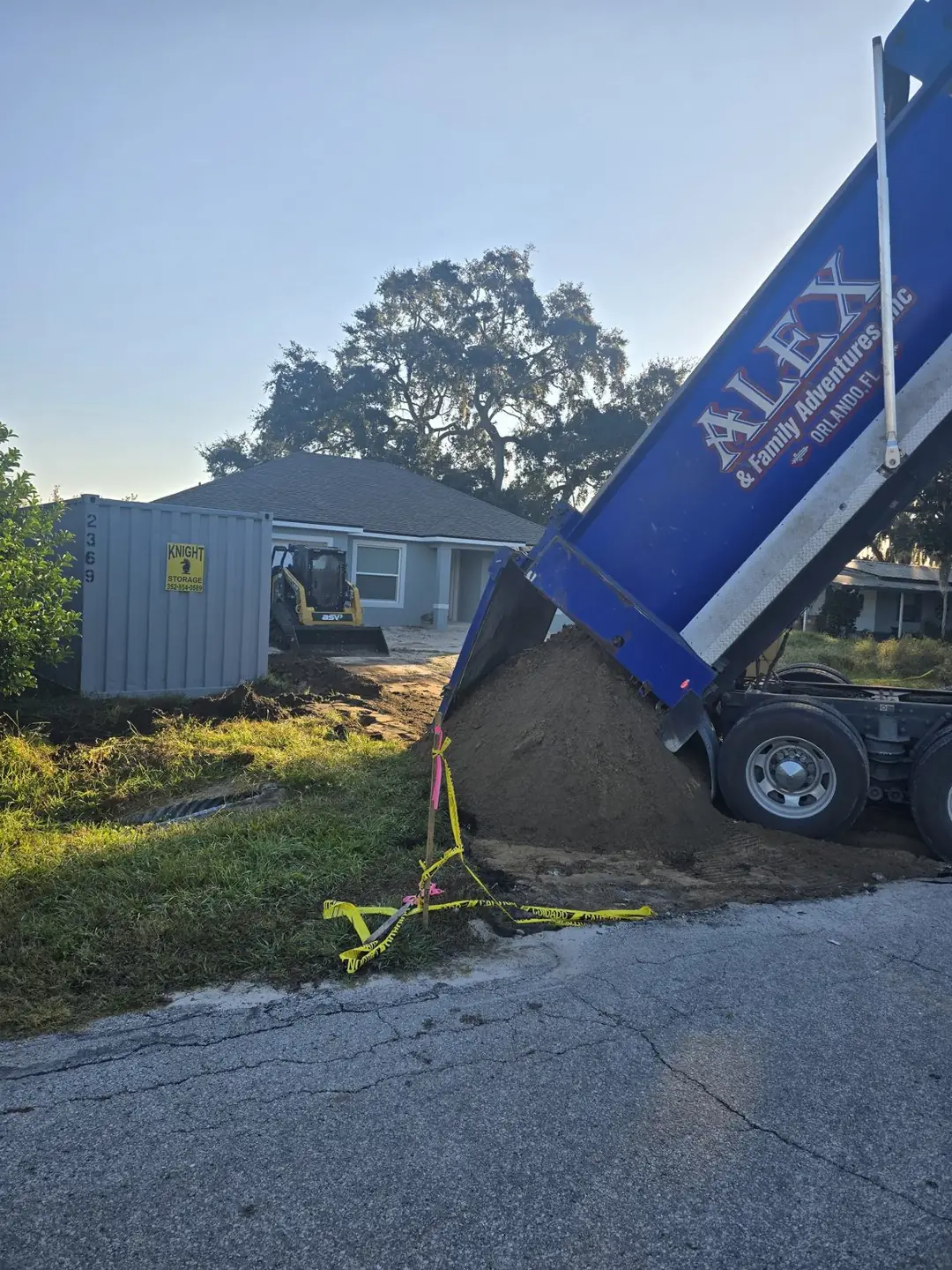Blue Alex and Family Trucking dump truck unloading fill dirt at a new home construction site near Orlando, Florida