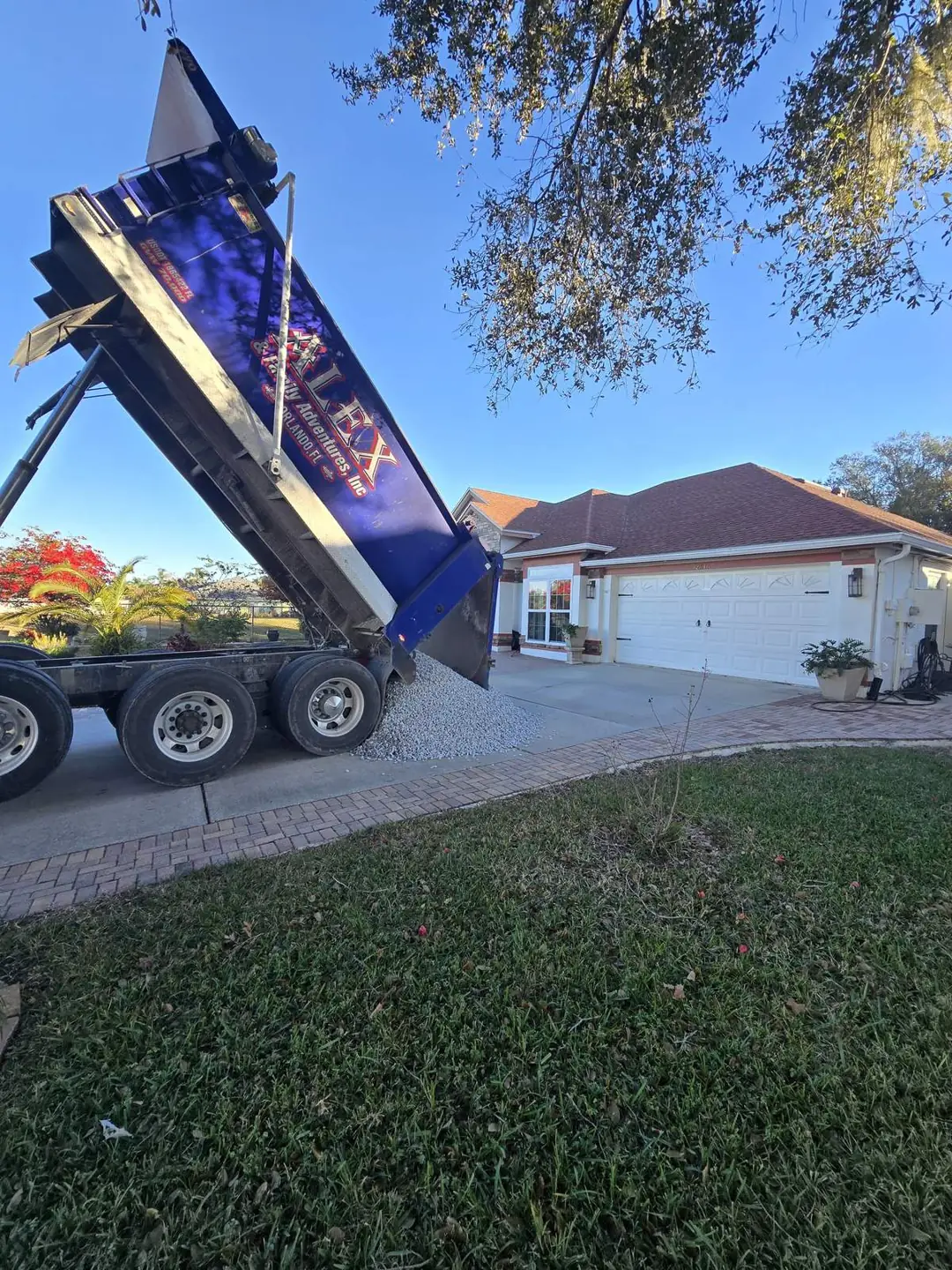 Alex and Family Trucking dump truck with its bed raised, sliding a load of gravel onto a home driveway in Central Florida