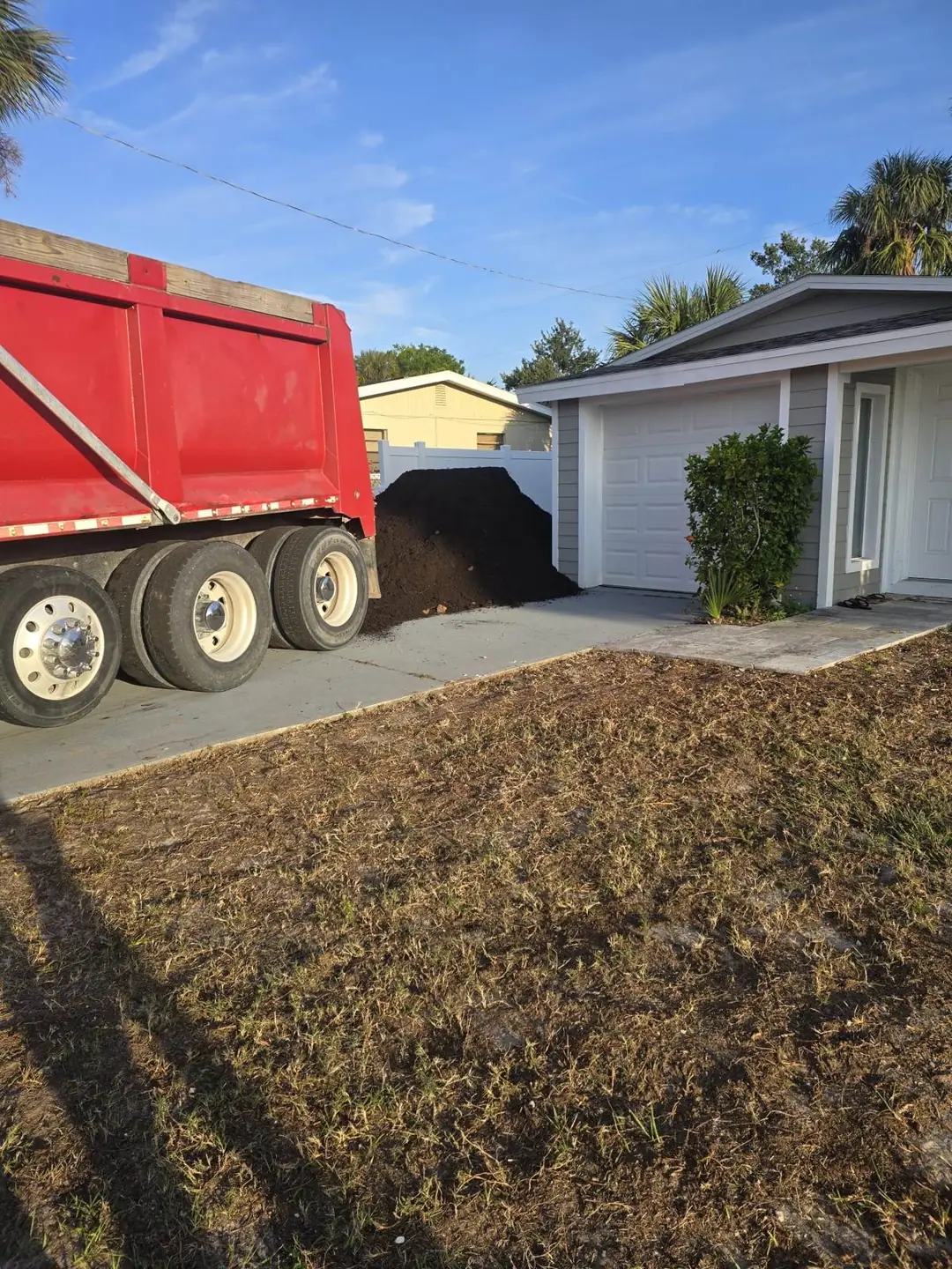 Red dump truck beside a mound of black topsoil delivered on a driveway for a lawn regrade in Central Florida