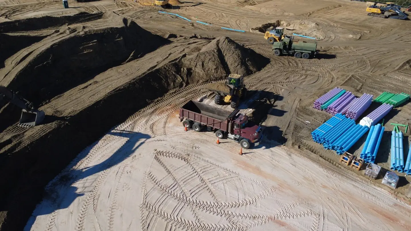 Aerial view of a dump truck being loaded with fill dirt by a front-end loader at a Central Florida construction site