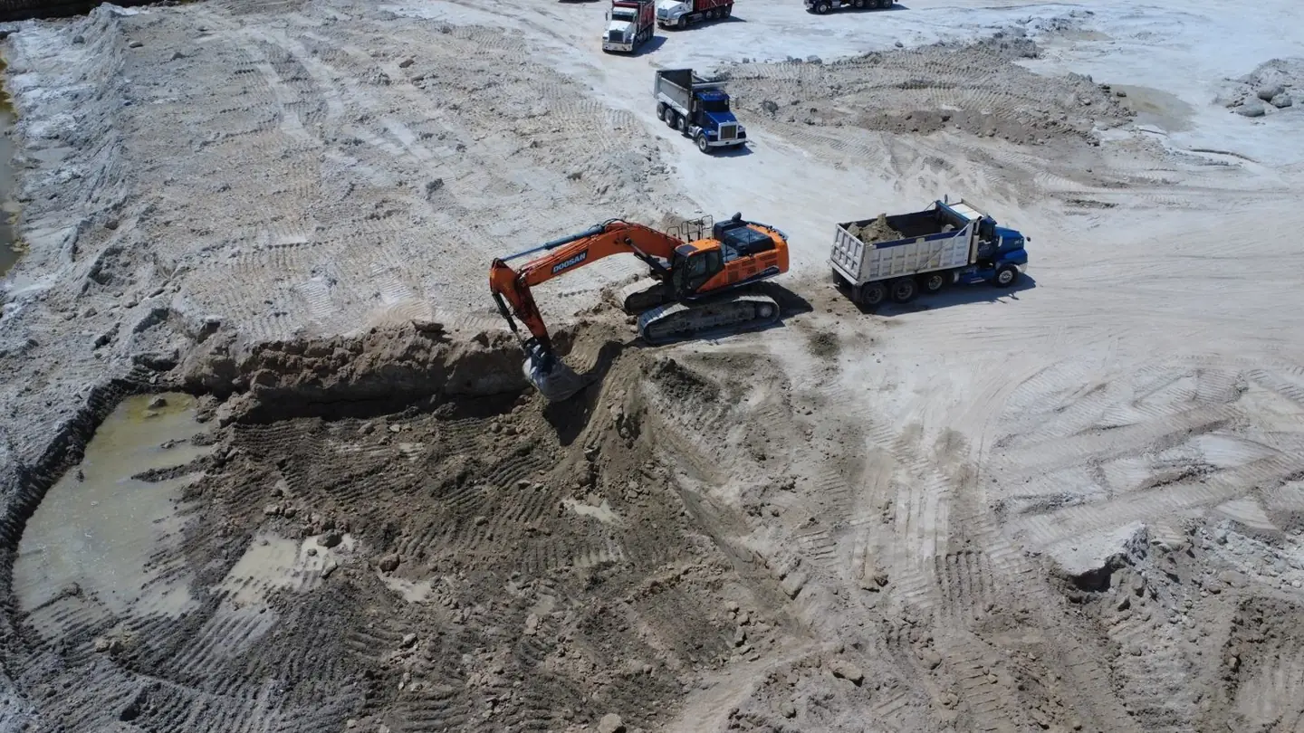 Excavator loading sand and gravel into dump trucks at an Orlando, Florida excavation site