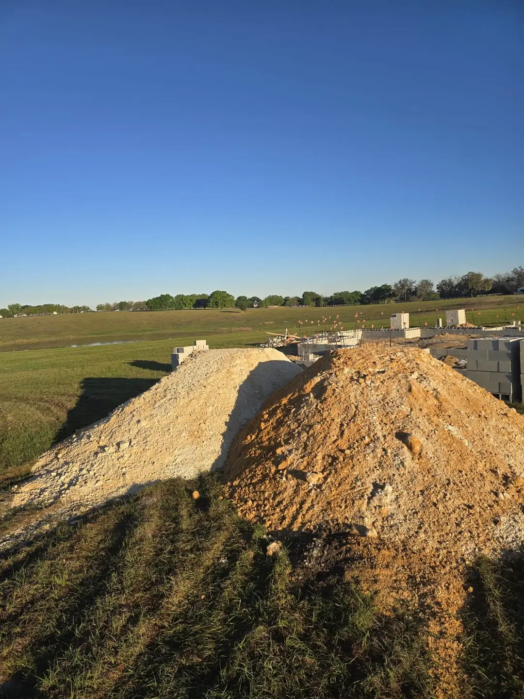 Stockpiles of white lime rock and orange fill dirt beside a block foundation at a Central Florida home construction site